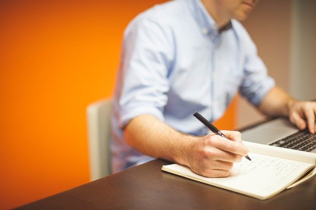 man writing next to computer